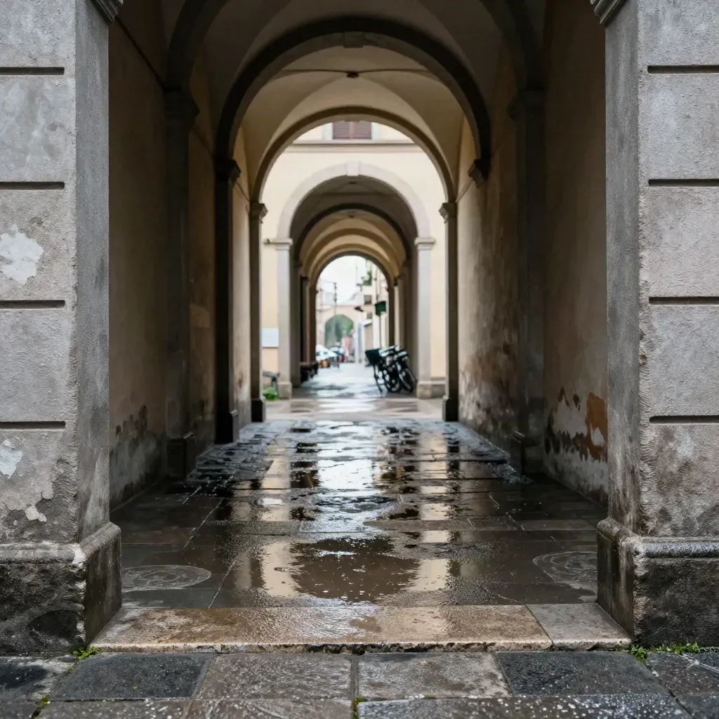 Portico bolognese bagnato dopo la pioggia, riflessi sulle arcate e biciclette sul fondo.